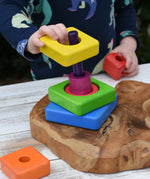 Child's hands are shown playing with a colorful wooden nesting shape-sorting toy from the Bajo Puzzle Stacker Tower.