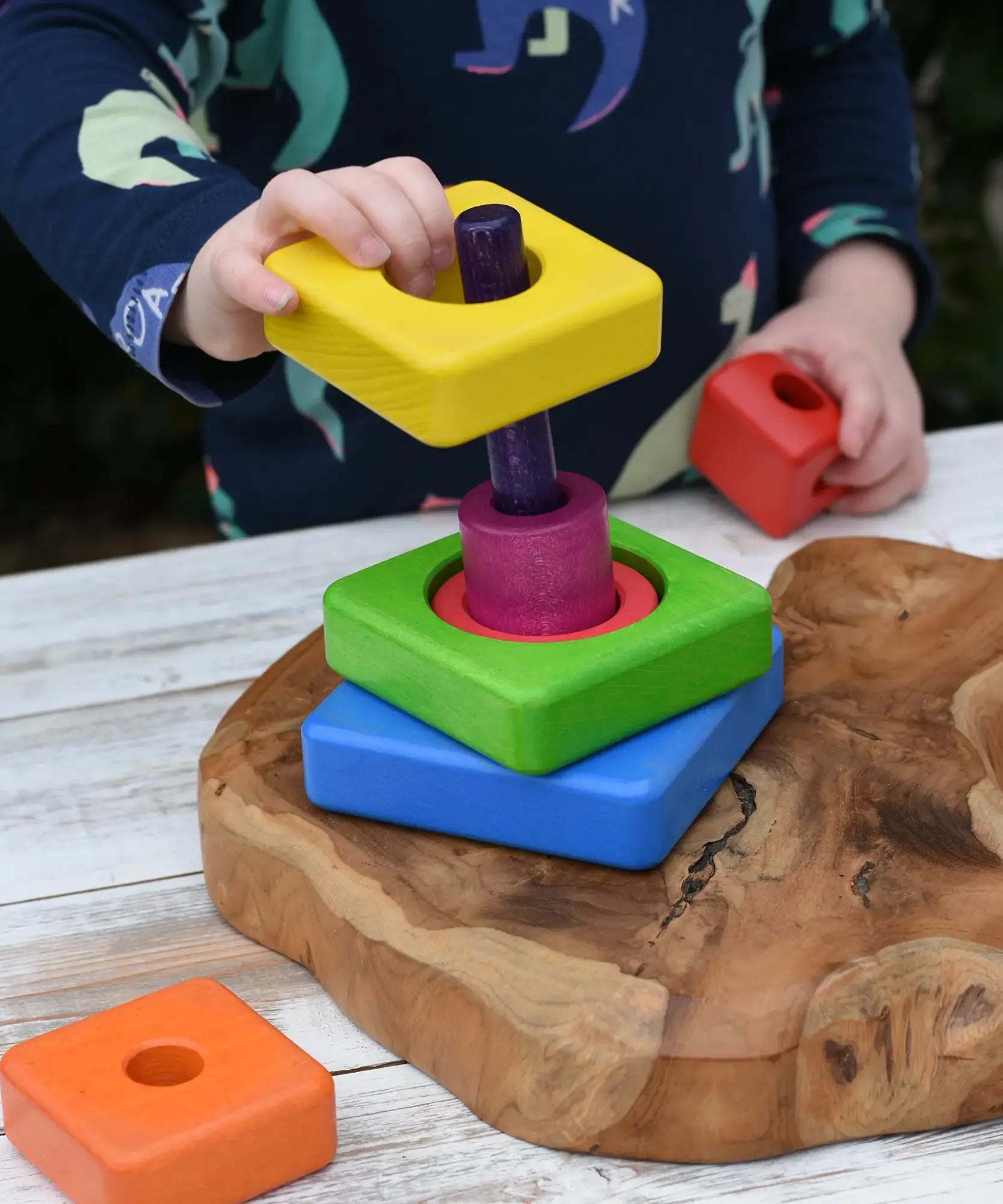 Child's hands are shown playing with a colorful wooden nesting shape-sorting toy from the Bajo Puzzle Stacker Tower.