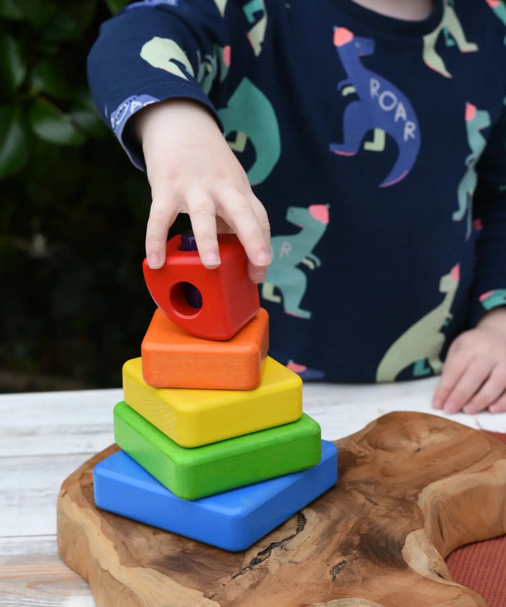 Child's hand stacks the pieces from the Bajo Puzzle Stacker Tower.