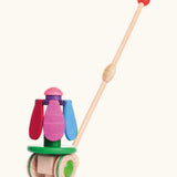 Bajo wooden rainbow flower push along toy on a green base with unpainted wheels and a long handle.