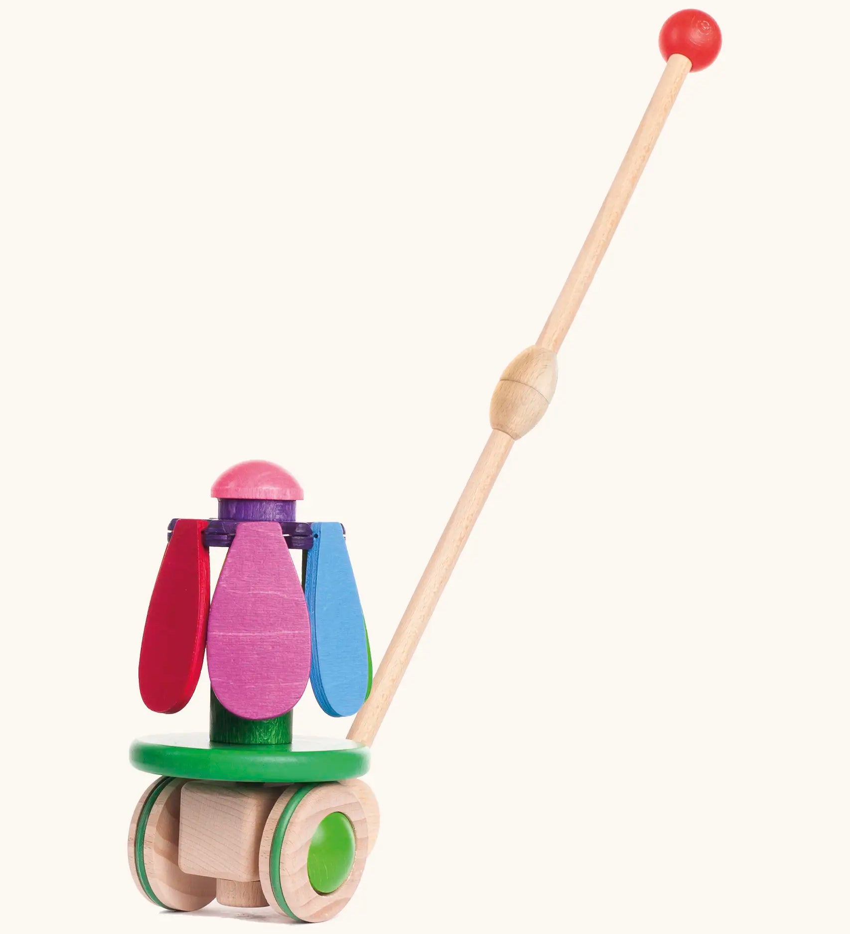 Bajo wooden rainbow flower push along toy on a green base with unpainted wheels and a long handle.