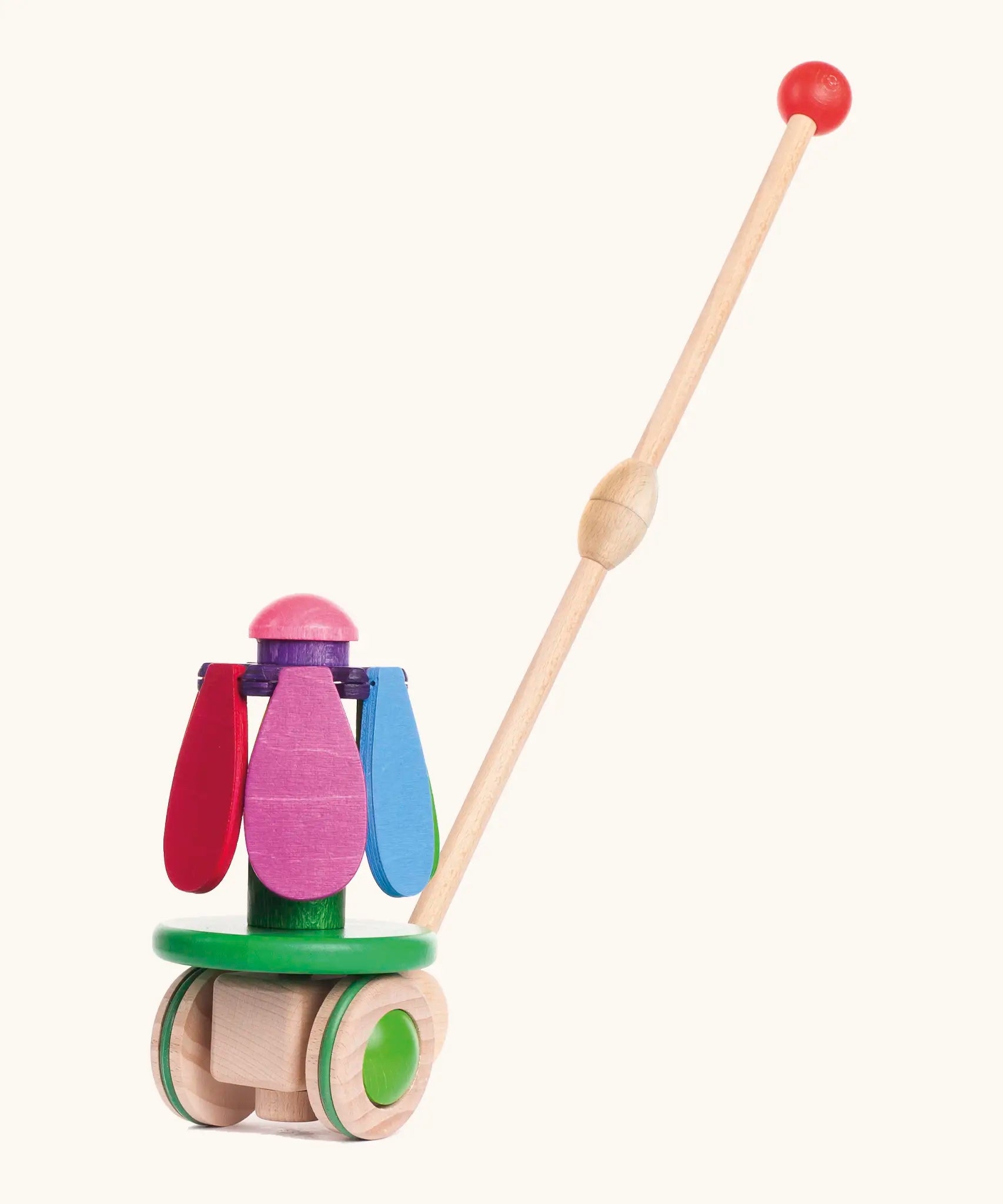 Bajo wooden rainbow flower push along toy on a green base with unpainted wheels and a long handle.