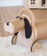 Bajo Ride On Wooden Dog with 4 wheels, working steering, a long nose and black felted ears and button eyes.