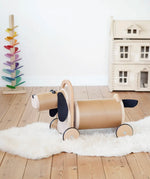Bajo Ride On Wooden Dog with 4 wheels and black felt tail and ears, a sit on barrel shaped sit on toy with working steering, in the Babipur playroom.