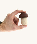An adult hand holding one of the smallest mushroom piece from the Bajo wooden mushroom shape sorter available at Babipur showing scale