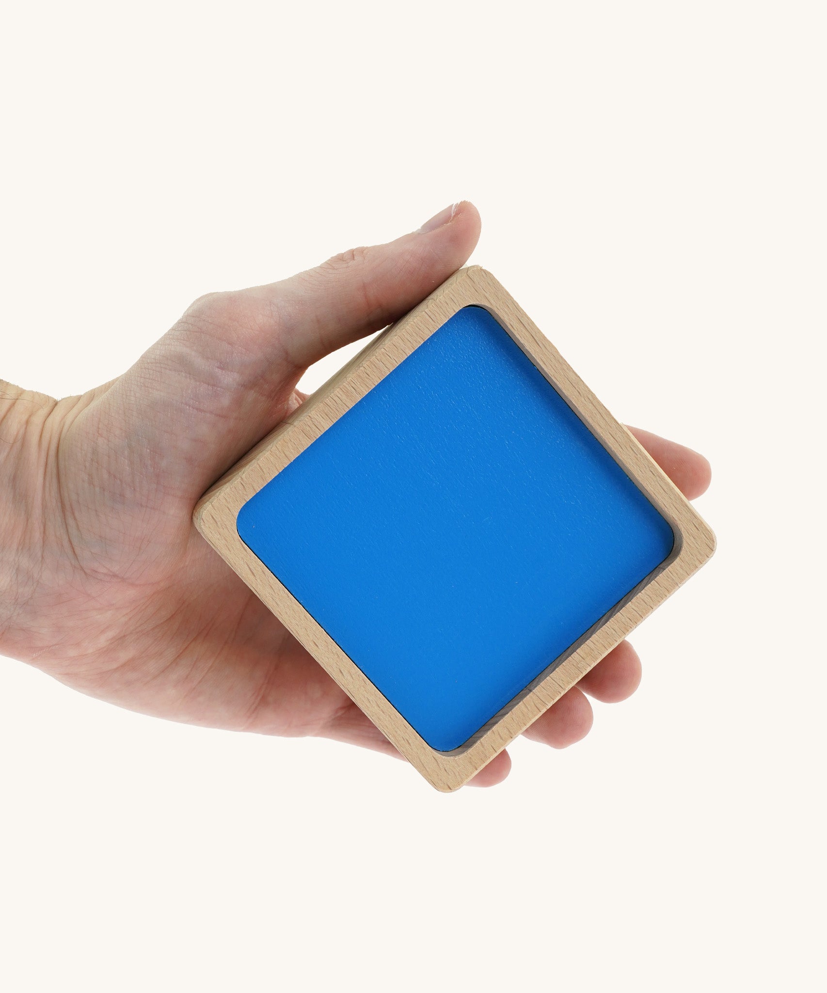 An adult hand holding the biggest wooden square block from the Bajo squaremide sensory blocks available at Babipur. This block has a blue base