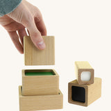 An adult hand placing a wooden block from the A tower stack made Bajo squaremide sensory blocks available at Babipur to build a tower