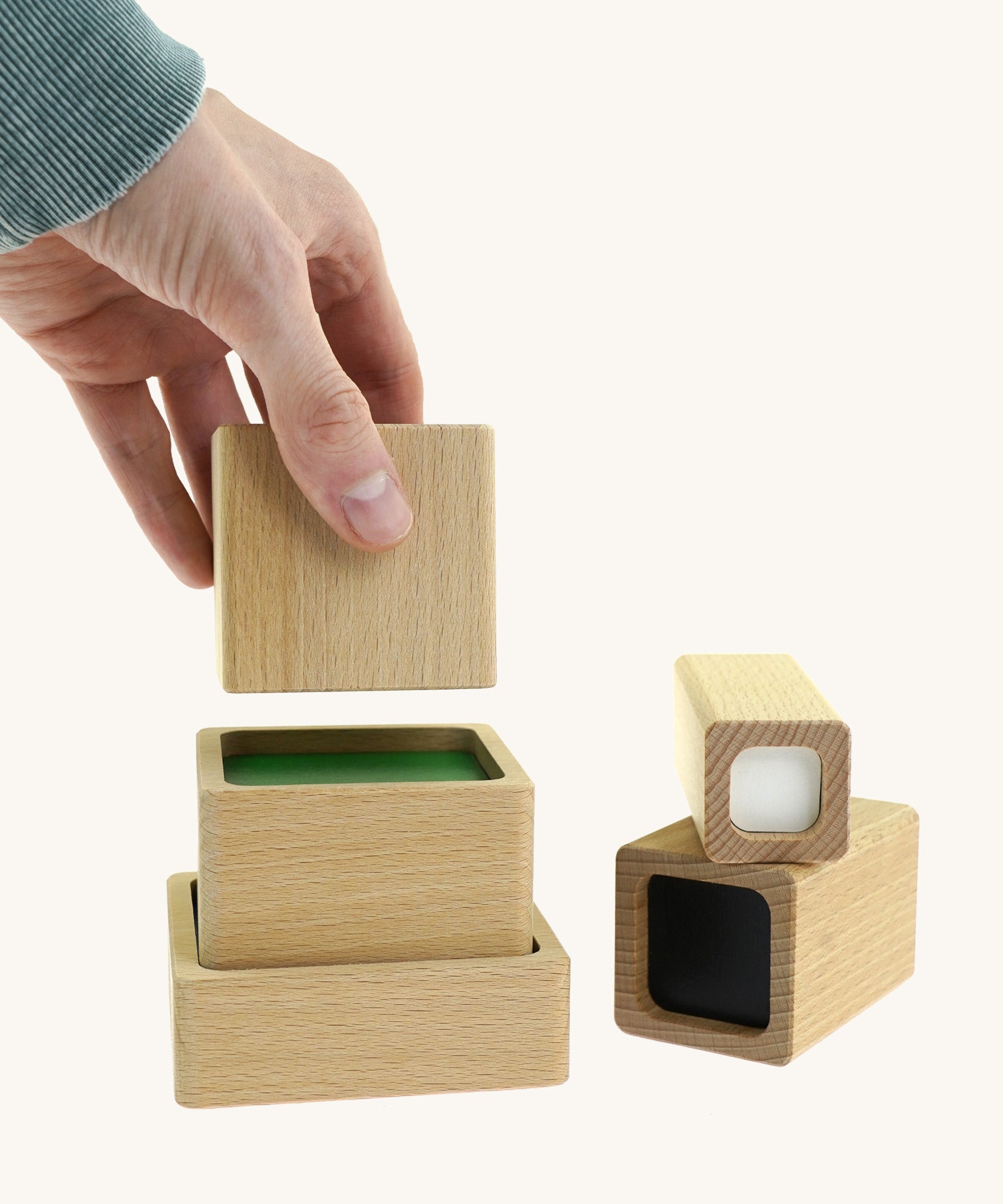 An adult hand placing a wooden block from the A tower stack made Bajo squaremide sensory blocks available at Babipur to build a tower