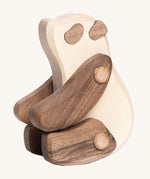 The Tobe Wooden Panda baby toy is sitting down on its back legs. It is a beautifully crated panda in two tone wood, with a white body, dark brown arms and legs, dark brown ears and eye patches. This wonderful wooden toy has movable arms and legs, and is on a cream background