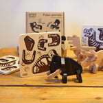 The Bajo Puzzle & Sorter - Black Oak Mammoth stood in front of its wooden puzzled board. The puzzle board has drawn on mammoth bones 