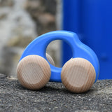 Bajo handmade wooden beetle style car in blue and available at Babipur. Can e push or pull along - photo on a stone wall.
