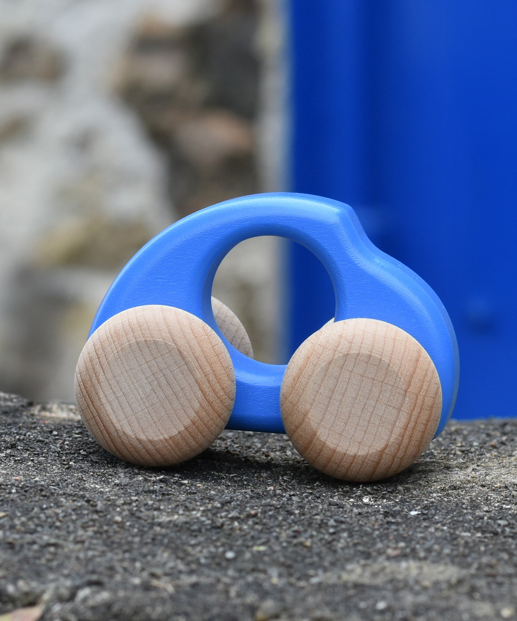 Bajo handmade wooden beetle style car in blue and available at Babipur. Can e push or pull along - photo on a stone wall.