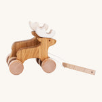 Bajo Wooden Pull Along Jumping Reindeer, is a beautiful children's toy of two natural wooden reindeer with wooden wheels and white antlers, and a wooden rectangle piece to pull along the reindeer which is attached to the reindeer with white string. The image is on a cream background