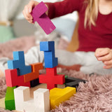 Child stacking different Bajo wooden coloured Pentomino puzzle blocks on a pink rug