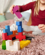 Child stacking different Bajo wooden coloured Pentomino puzzle blocks on a pink rug