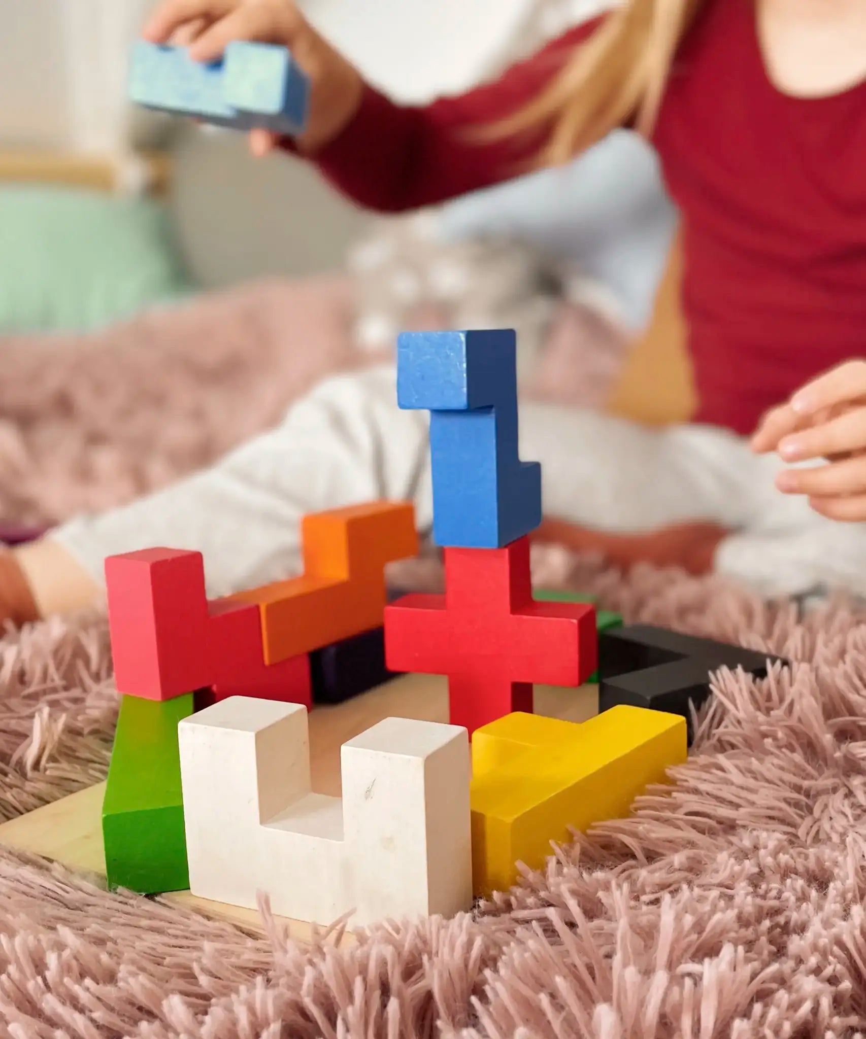 Child building a tower using different Bajo wooden coloured Pentomino puzzle blocks