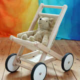 A  Bajo Toys wooden toy stroller with white wheels and a beige Senger teddy bear sitting inside, placed on a wooden floor against a colorful rainbow-striped backdrop.