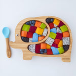 Eco Rascals Elephant Bamboo Suction Plate filled with colourful cubed fruit to look like Elmer the Elephant, with a bamboo and blue silicone baby spoon. 