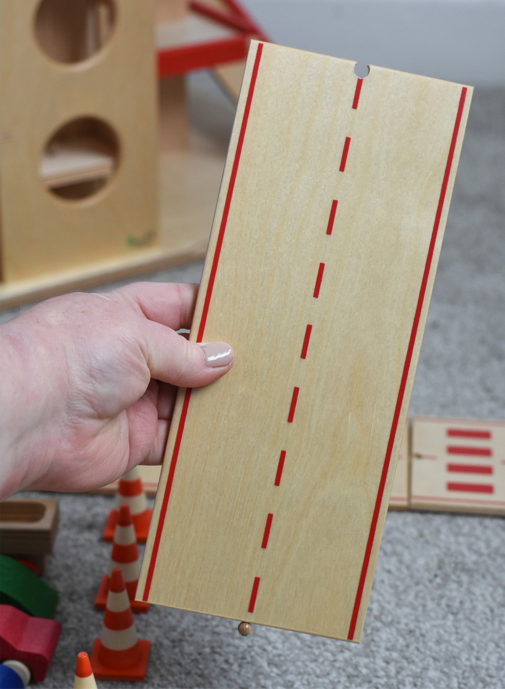 A person holding a straight piece of the wooden toy road set by Beck-Holzspielzeug.