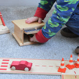 A child opening the canopy door of the wooden toy parking garage by Beck Holzspielzeug, putting mini wooden toy cars inside.