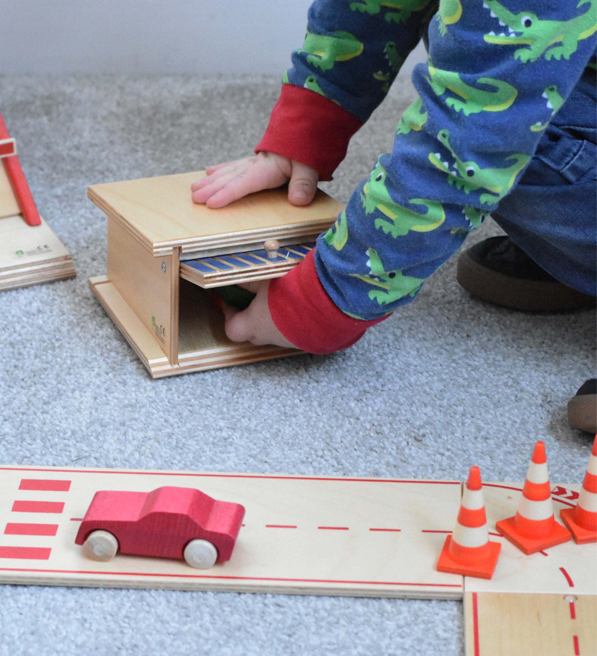A child opening the canopy door of the wooden toy parking garage by Beck Holzspielzeug, putting mini wooden toy cars inside.