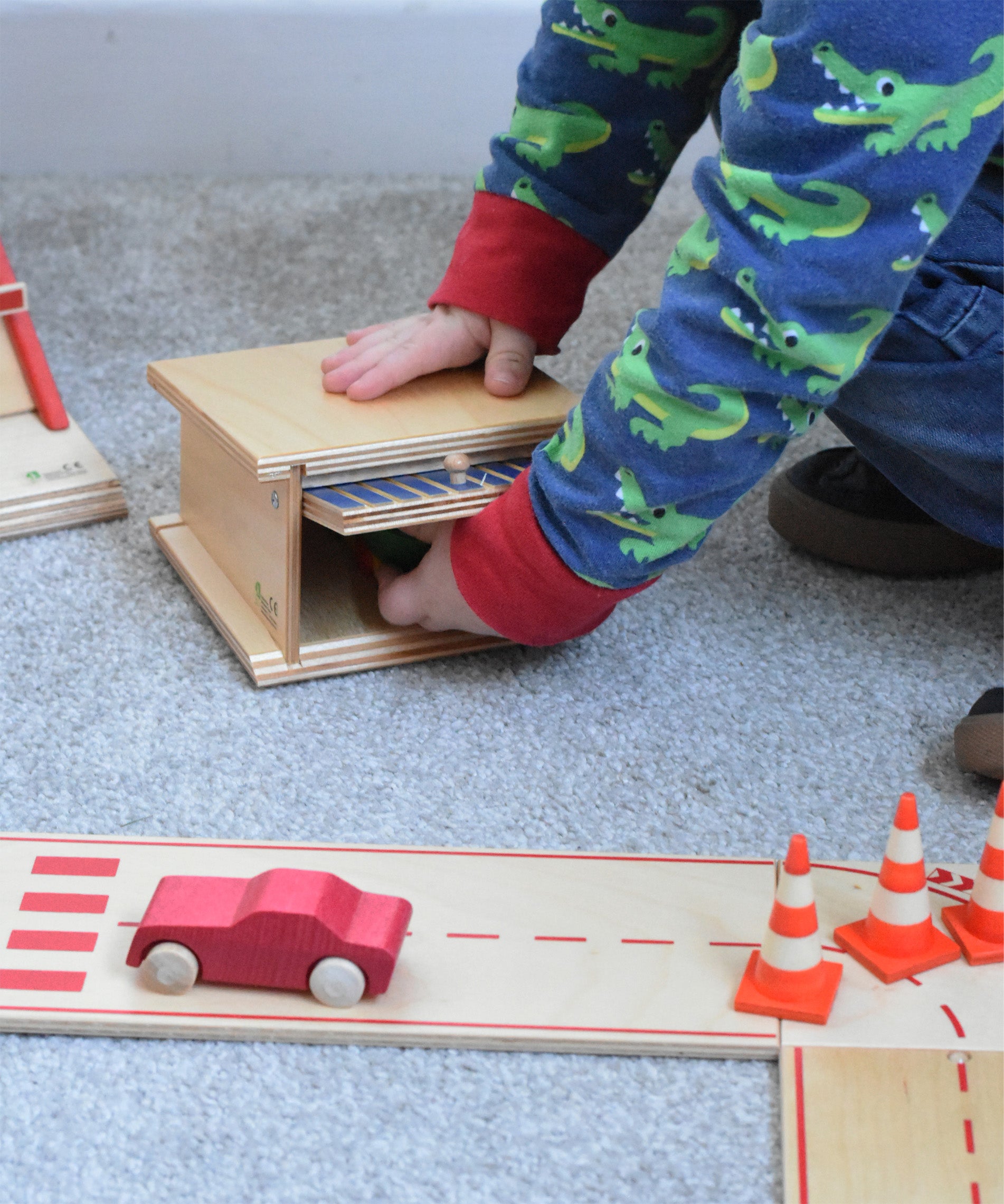 A child opening the canopy door of the wooden toy parking garage by Beck Holzspielzeug, putting mini wooden toy cars inside.