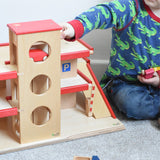 A child playing with the Beck Holzspielzeug wooden toy multi-storey car park, along with little toy cars. 