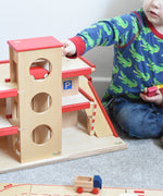 A child playing with the Beck Holzspielzeug wooden toy multi-storey car park, along with little toy cars. 