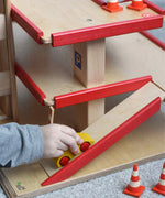 A child pushing a wooden toy car up the wooden multi-storey car park by Beck-Holzspielzeug