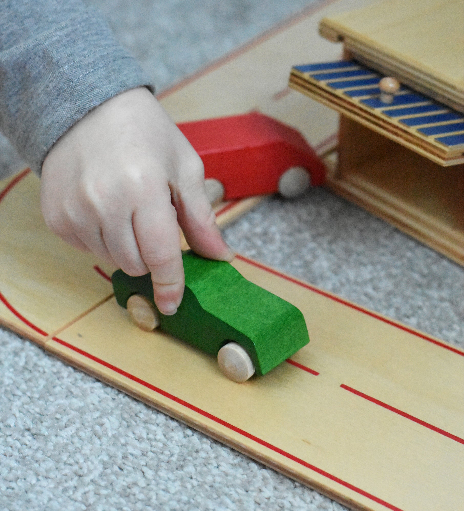 A child pushing a little wooden toy passenger car along he wooden toy road system by Beck-Holzspielzeug.