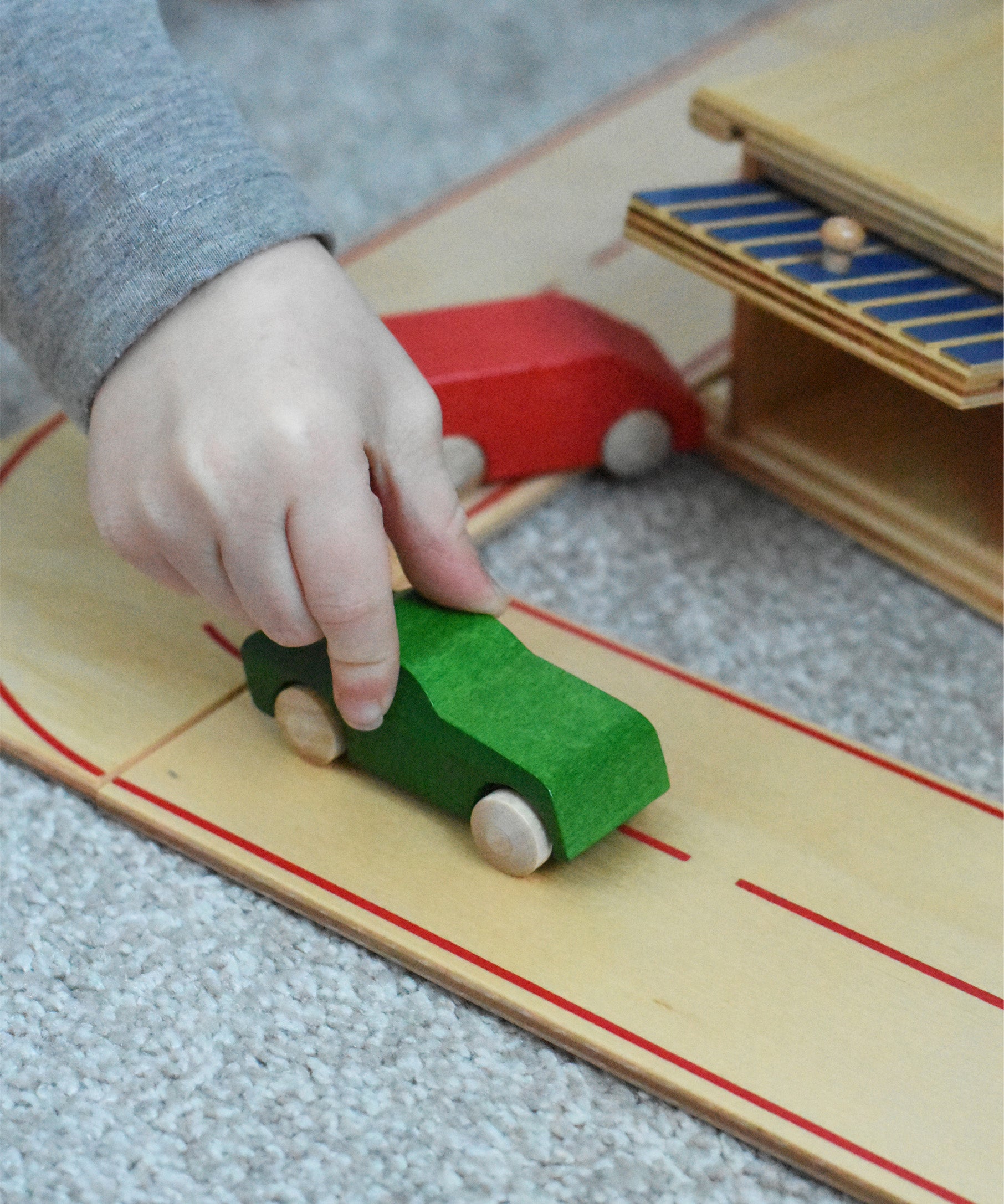 A child pushing a little wooden toy passenger car along he wooden toy road system by Beck-Holzspielzeug.