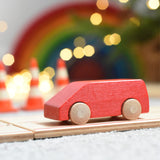 The Beck Holzspielzeug mini wooden toy van, driving along the wooden road track with traffic cones, twinkling lights, and a Grimm's rainbow in the background. 