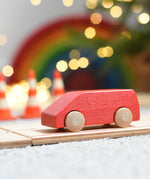 The Beck Holzspielzeug mini wooden toy van, driving along the wooden road track with traffic cones, twinkling lights, and a Grimm's rainbow in the background. 