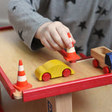 A child playing with the wooden toy multi-storey car park by Beck-Holzspielzeug, placing mini traffic cones around a wooden toy car. 