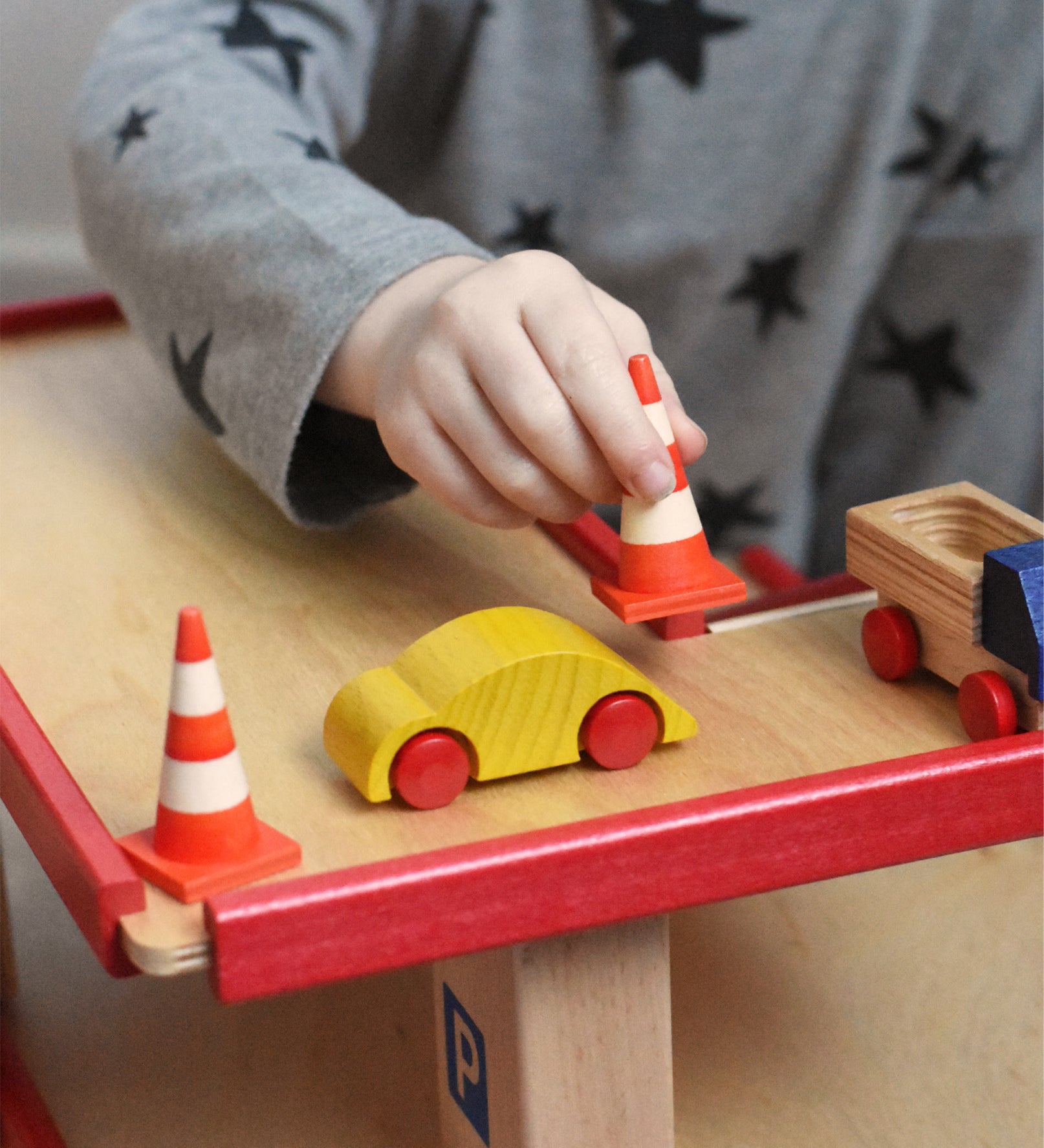 A child playing with the wooden toy multi-storey car park by Beck-Holzspielzeug, placing mini traffic cones around a wooden toy car. 
