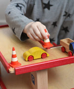 A child playing with the wooden toy multi-storey car park by Beck-Holzspielzeug, placing mini traffic cones around a wooden toy car. 
