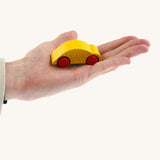 An adult hand holding the Beck wooden speedy race car toy in yellow available at Babipur showing scale