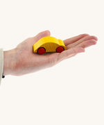 An adult hand holding the Beck wooden speedy race car toy in yellow available at Babipur showing scale