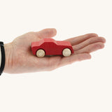 An adult hand holding the Beck wooden toy passenger car in red available at Babipur showing scale