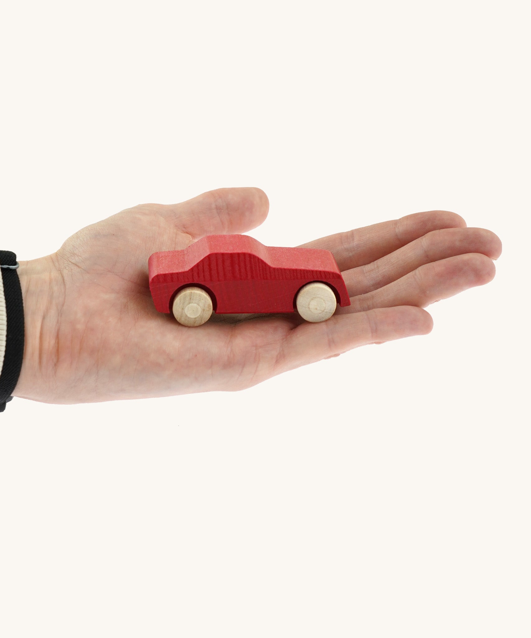 An adult hand holding the Beck wooden toy passenger car in red available at Babipur showing scale