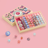 Different sized marbles from the Billes & Co butterfly anamorphic set on a pink surface with a pink butterfly box in the background.