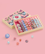 Different sized marbles from the Billes & Co butterfly anamorphic set on a pink surface with a pink butterfly box in the background.