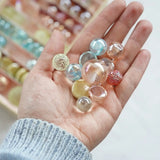 Adult hand holding different sized glass marbles from the Billes & Co pink fairy marble set 
