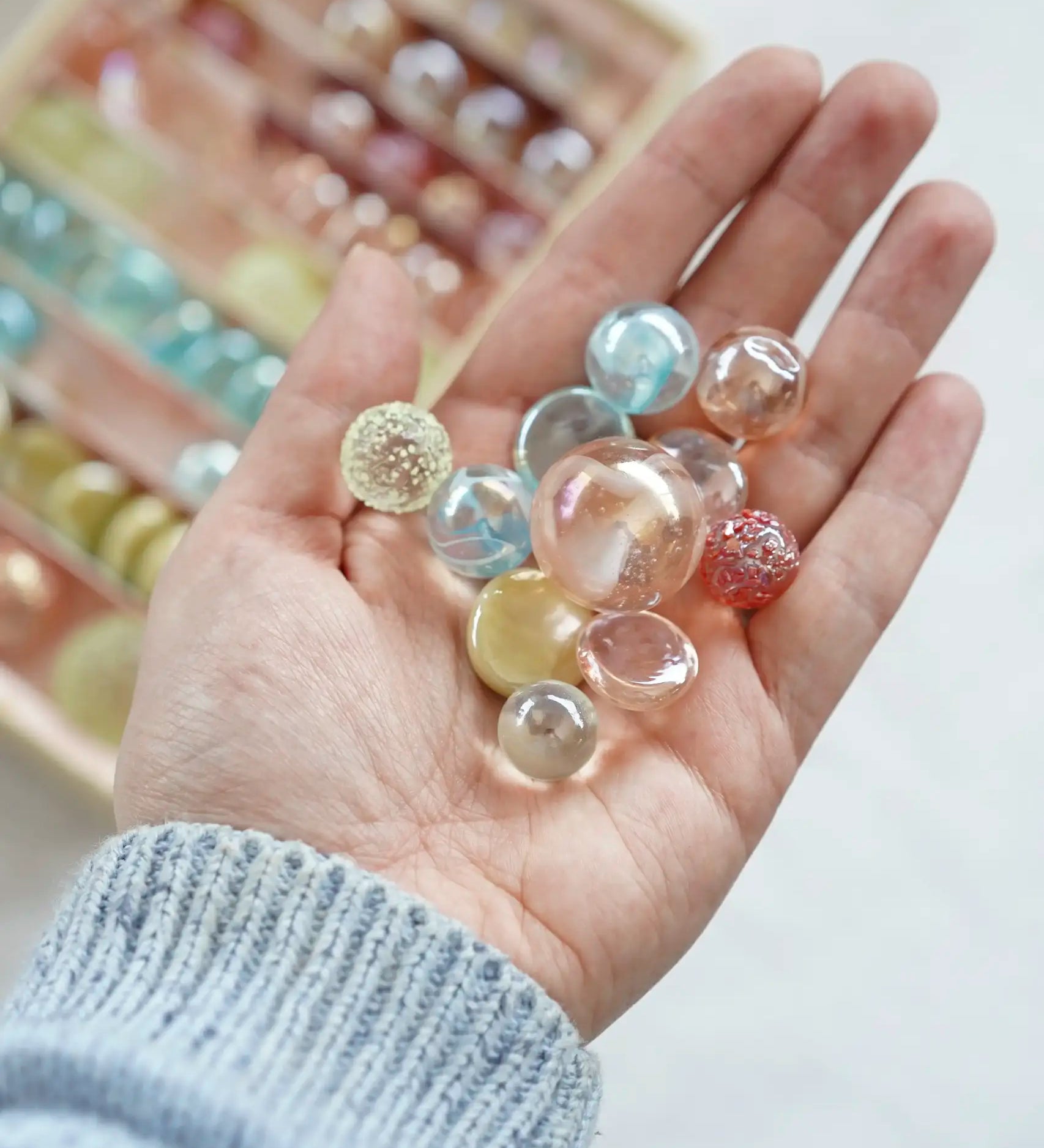 Adult hand holding different sized glass marbles from the Billes & Co pink fairy marble set 
