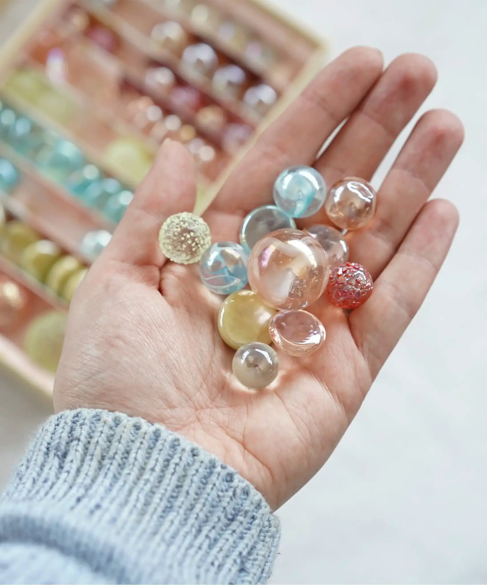 Adult hand holding different sized glass marbles from the Billes & Co pink fairy marble set 