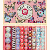 Billes & Co butterfly anamorphic glass marble set presented in a butterfly gift box. The marbles are lined up in order of size and pastel colours.