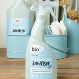 Bio-d 500ml all purpose sanitiser spray in fragrance free standing on a wooden surface with a 5L bottle in the background with cleaning products. This sanitiser spray is available at Babipur.