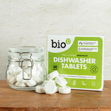 A pile of Bio-D dishwasher tablets in the water soluble film inside a glass jar standing next to the green box packaging. These dishwasher tablets are available at Babipur.