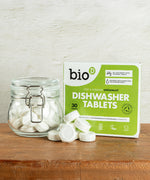 A pile of Bio-D dishwasher tablets in the water soluble film inside a glass jar standing next to the green box packaging. These dishwasher tablets are available at Babipur.
