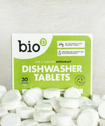 A pile of Bio-D dishwasher tablets in the water soluble film in front of it's packaging. These dishwasher tablets are available at Babipur.